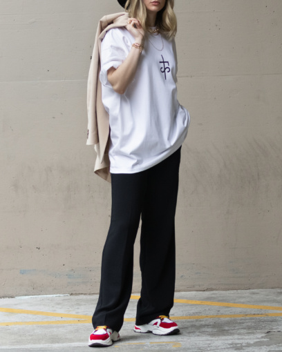 Model wearing black dress pants, colourful sneakers and white chest logo tshirt from The Foreign Sun